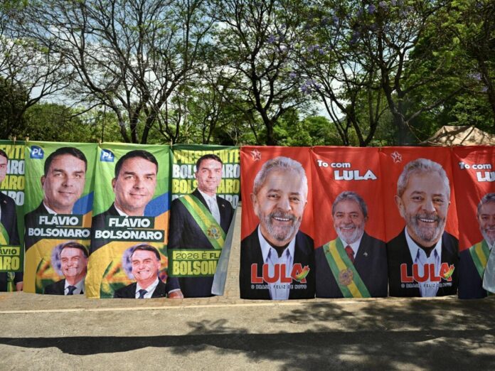 Unas banderas y toallas con la imagen del presidente de Brasil, Luiz Inácio Lula da Silva (drcha.), candidato a la reelección, y de su rival el senador Flávio Bolsonaro, puestas a la venta en una calle de Brasilia el 30 de septiembre de 2026 © Evaristo Sa / AFP
